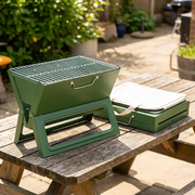Green foldable tabletop charcoal grill on an outdoor table